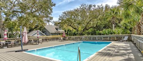 A wooden deck with a swimming pool, surrounded by trees and outdoor furniture.