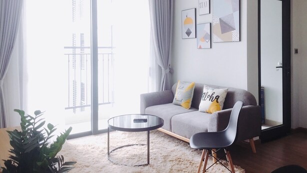 Een moderne woonkamer met een grijze bank, een ronde salontafel en een groot raam met gordijnen.