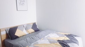 Een net opgemaakt bed met een bedspreide en kussens met een geometrisch patroon, een houten hoofdbord en een lijst met een bordje aan de muur.