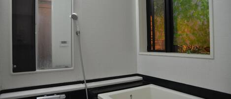 Een badkamer met een bad, een toilet en een raam met uitzicht op bomen.