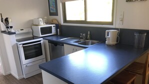 A kitchen with a microwave, toaster, oven, and sink. There is a window providing natural light. - Pauanui Beach House. (Pauanui)