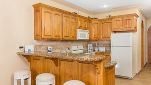 A kitchen with wooden cabinets, a granite countertop, a microwave, a coffee maker, and a refrigerator. - Casa Blanca CB-102 Let Me Count The Waves Beautiful View Condo (Puerto Peñasco)