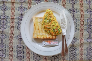 A plate with toast and scrambled eggs, a packet of seasoning, and a knife on a table with a patterned tablecloth. - The Tukad Gepuh Cottage (Penida Island)