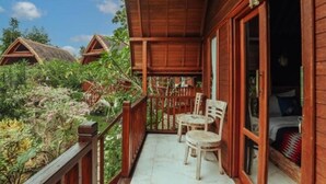 A wooden balcony with two chairs and a bed visible through the open door. - The Tukad Gepuh Cottage (Penida Island)