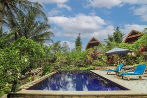 A pool area with lounge chairs and umbrellas, surrounded by lush greenery and palm trees. - The Tukad Gepuh Cottage (Penida Island)