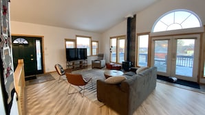 A spacious living room with a large flat-screen TV, comfortable seating, and large windows offering a view of the outdoors. - Capitol Reef Home with fast wi-fi and washer/dryer (Teasdale)