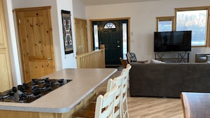 A modern kitchen with a central island, wooden chairs, a dining table, and a TV in the living area. - Capitol Reef Home with fast wi-fi and washer/dryer (Teasdale)