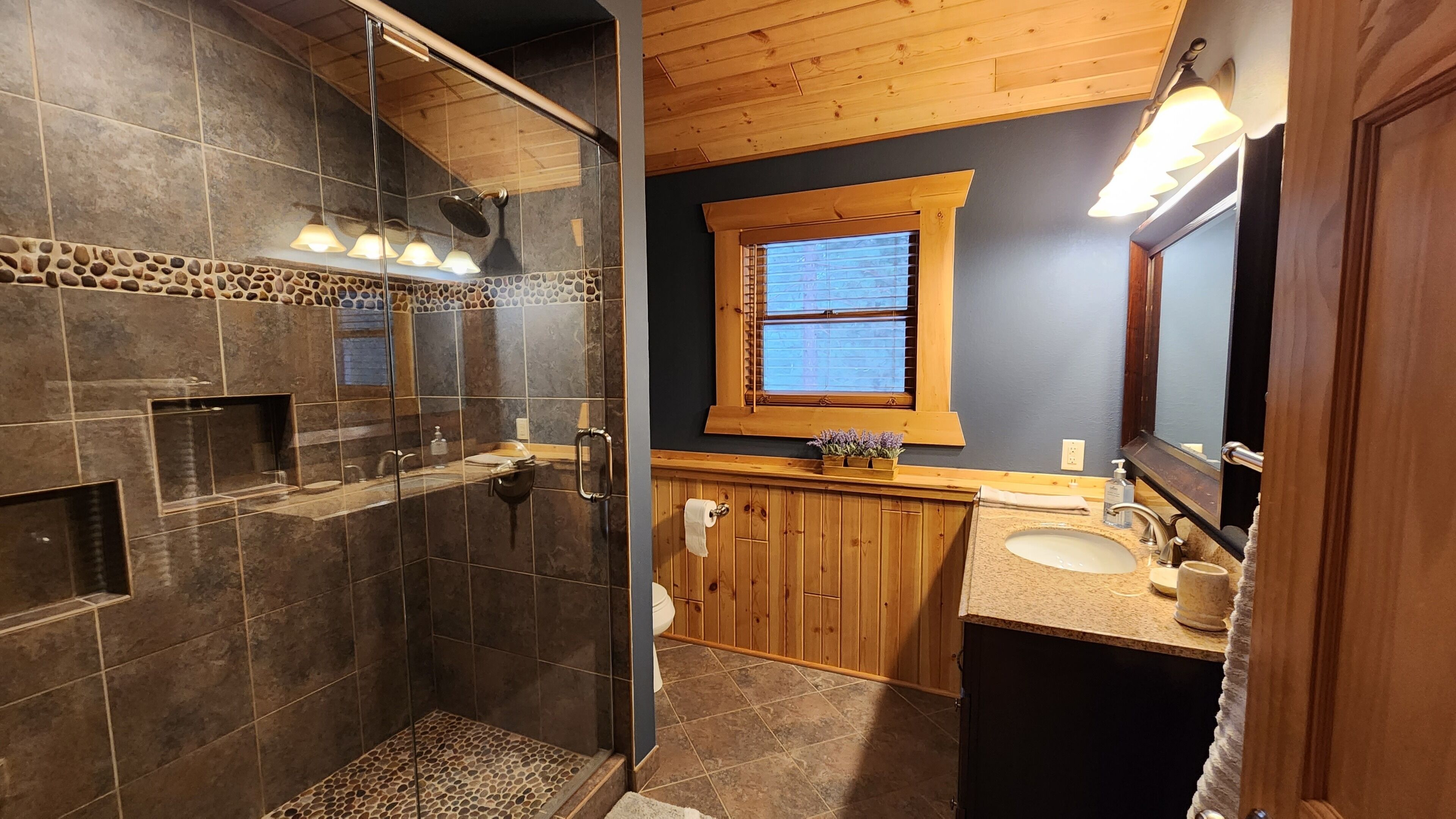 Un bagno con cabina doccia in vetro, mobile lavabo in legno e uno specchio grande.