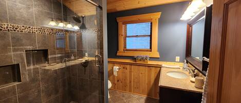 Un bagno con cabina doccia in vetro, mobile lavabo in legno e uno specchio grande.