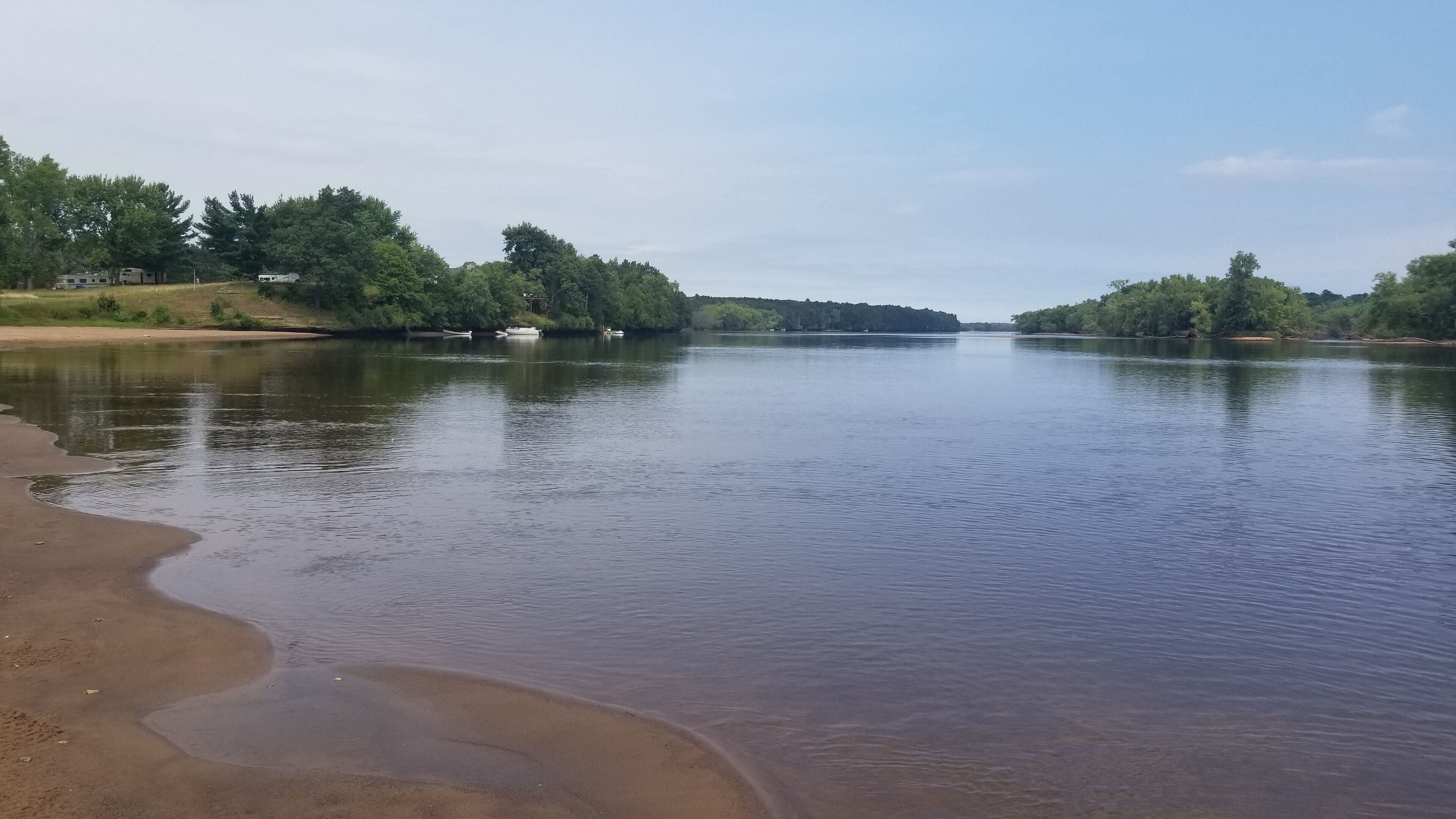 A calm river with a sandy bank and trees in the background.