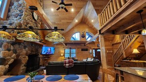 A cozy cabin interior with a stone fireplace, wooden ceiling, and a large window. - 🏞Secluded Log Cabin Near Wisconsin Dells & Wisconsin River • Fireplace • Ski 🏕 (Lyndon Station)