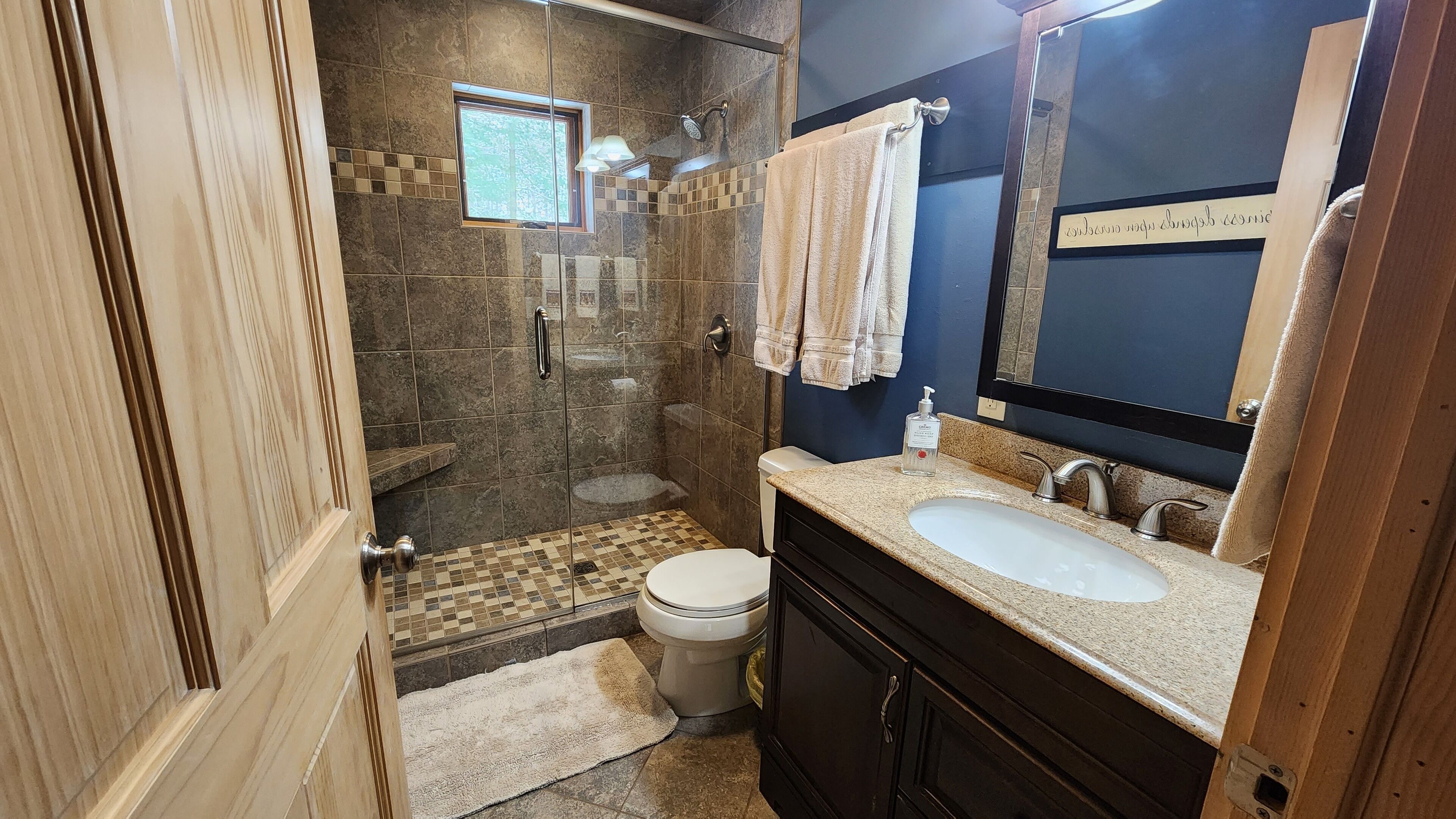 A bathroom with a shower, toilet, sink, and a mirror.