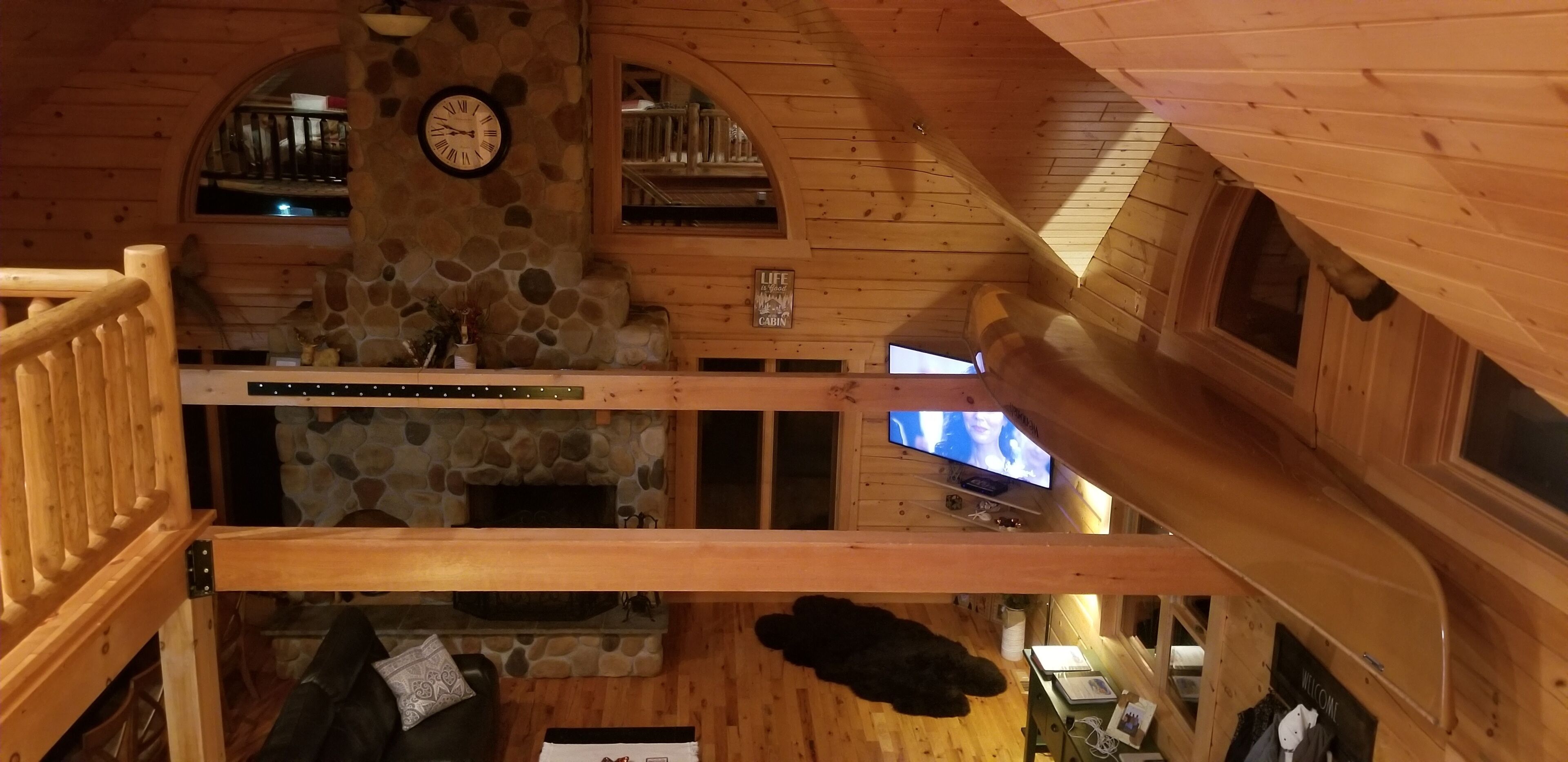 L’intérieur d’une cabane avec une cheminée en pierre, des murs en bois, une horloge et un téléviseur.