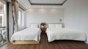 A hotel room with two beds, wooden flooring, a large window with curtains, and a small bedside table with a vase of flowers. - Lakeside House - Hanoi (Hanoi)