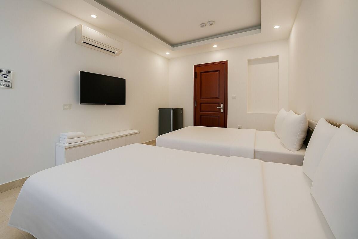 A hotel room with two beds, a TV, a wooden door, and an air conditioning unit.