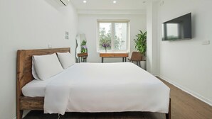 A bedroom with a wooden bed, a desk, a chair, a TV, and a window with a view of greenery. - Lakeside House - Hanoi (Hanoi)