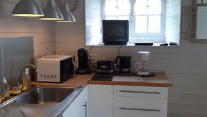 A compact kitchen with white cabinets, a sink, a toaster, a coffee maker, and a window with curtains.