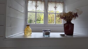 A window with white shutters, a yellow bottle, a clear glass container, and a vase with dried flowers.
