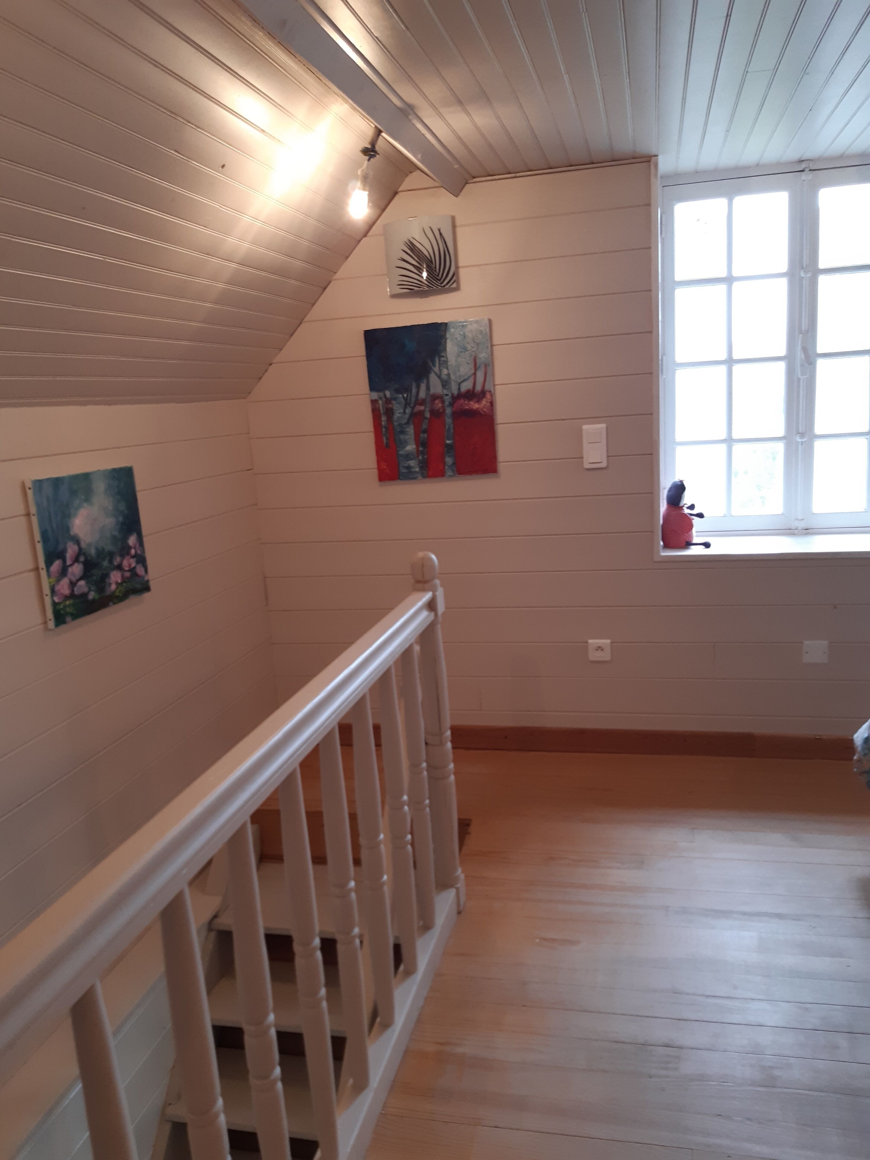 Quarto com piso de madeira, corrimão branco e janela com vista.