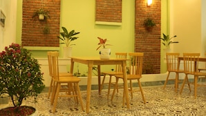 A dining area with a brick wall, green walls, wooden chairs, a table with a vase, and potted plants. - Lam Garden Boutique Homestay (Hue)