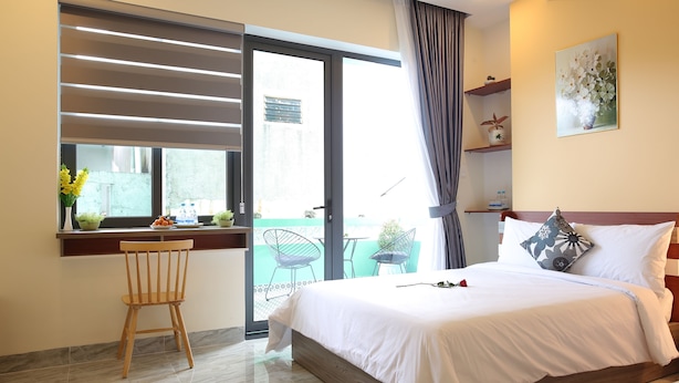 A hotel room with a bed, a desk with a chair, a window with blinds, and a balcony with chairs. - Lam Garden Boutique Homestay (Hue)