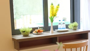 A room with a wooden chair, a window with a view, a shelf with plants and water bottles. - Lam Garden Boutique Homestay (Hue)