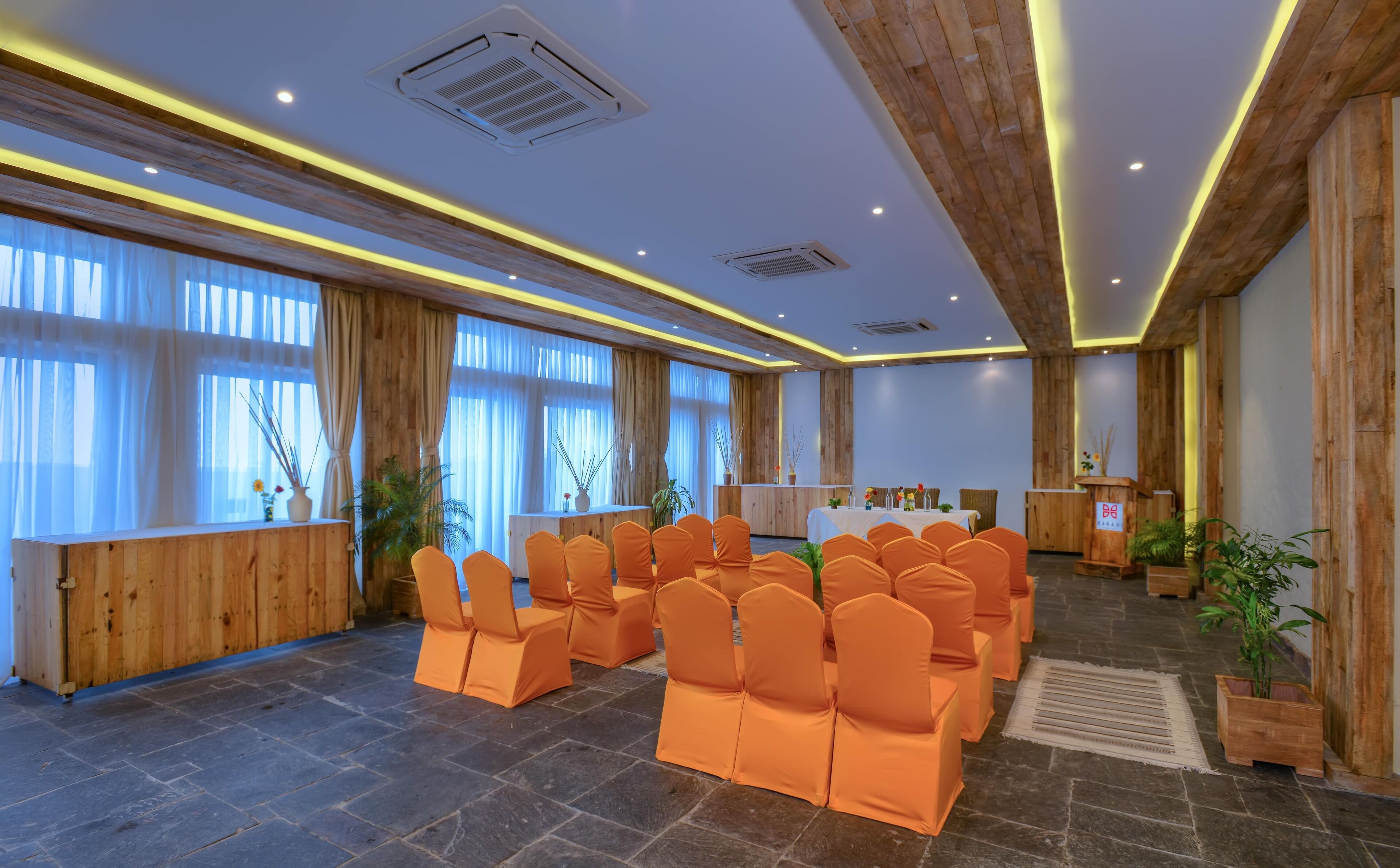 A conference room with orange chairs arranged in rows, wooden paneling on the walls, and a podium with a microphone.
