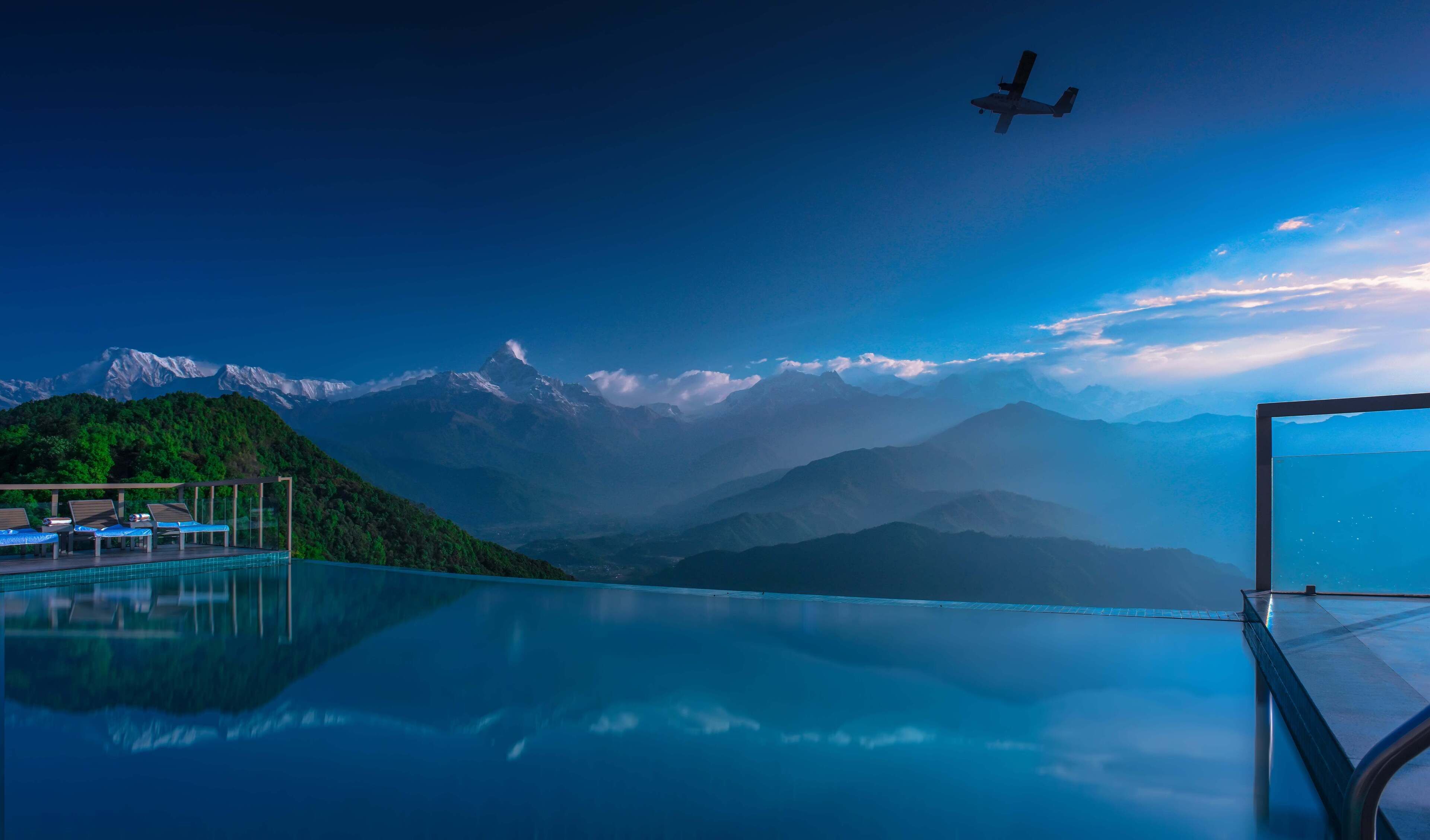 A pool with a mountain view, lounge chairs, and a clear sky.