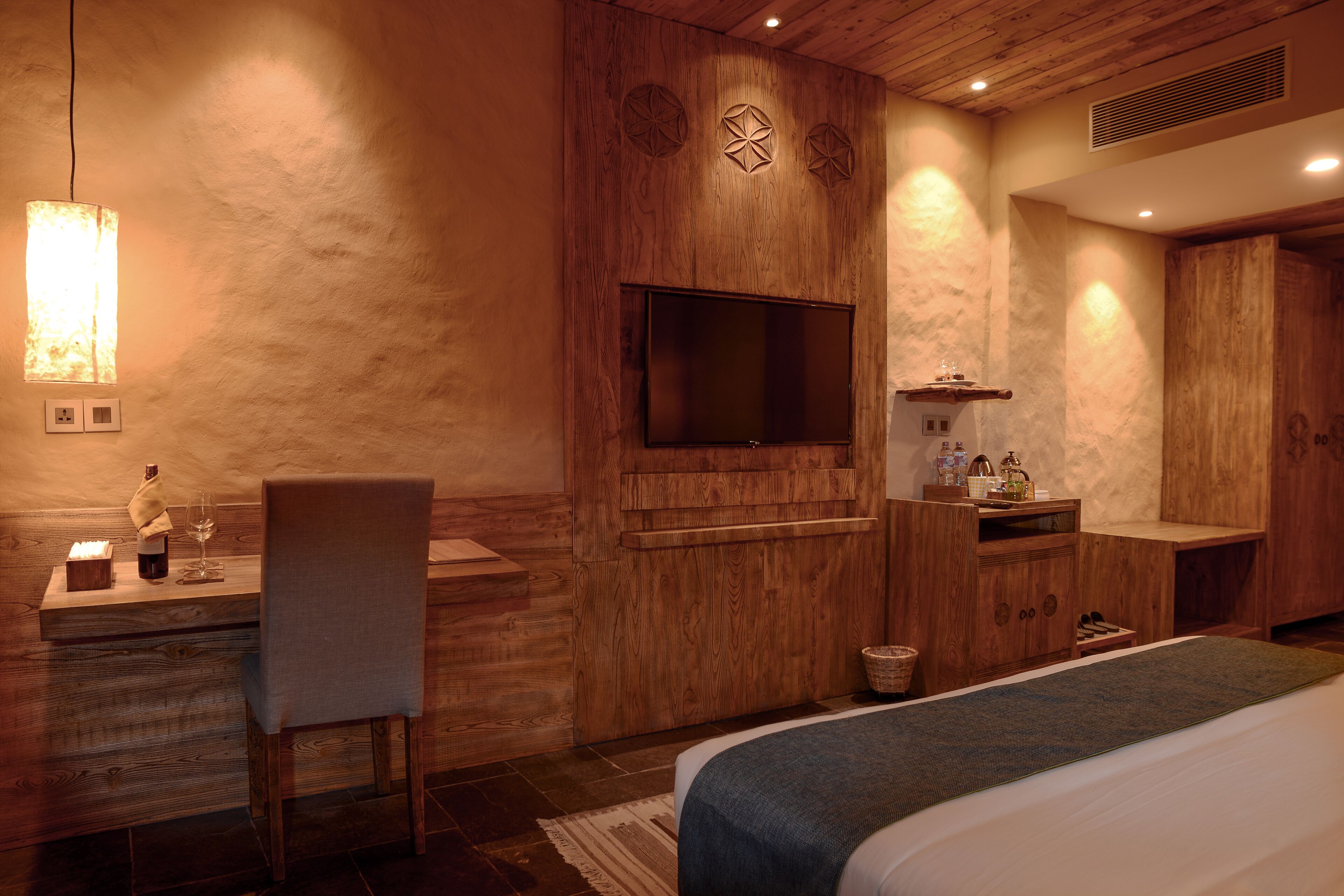 A hotel room with a wooden desk, chair, flat-screen TV, and a bed with a blue blanket.