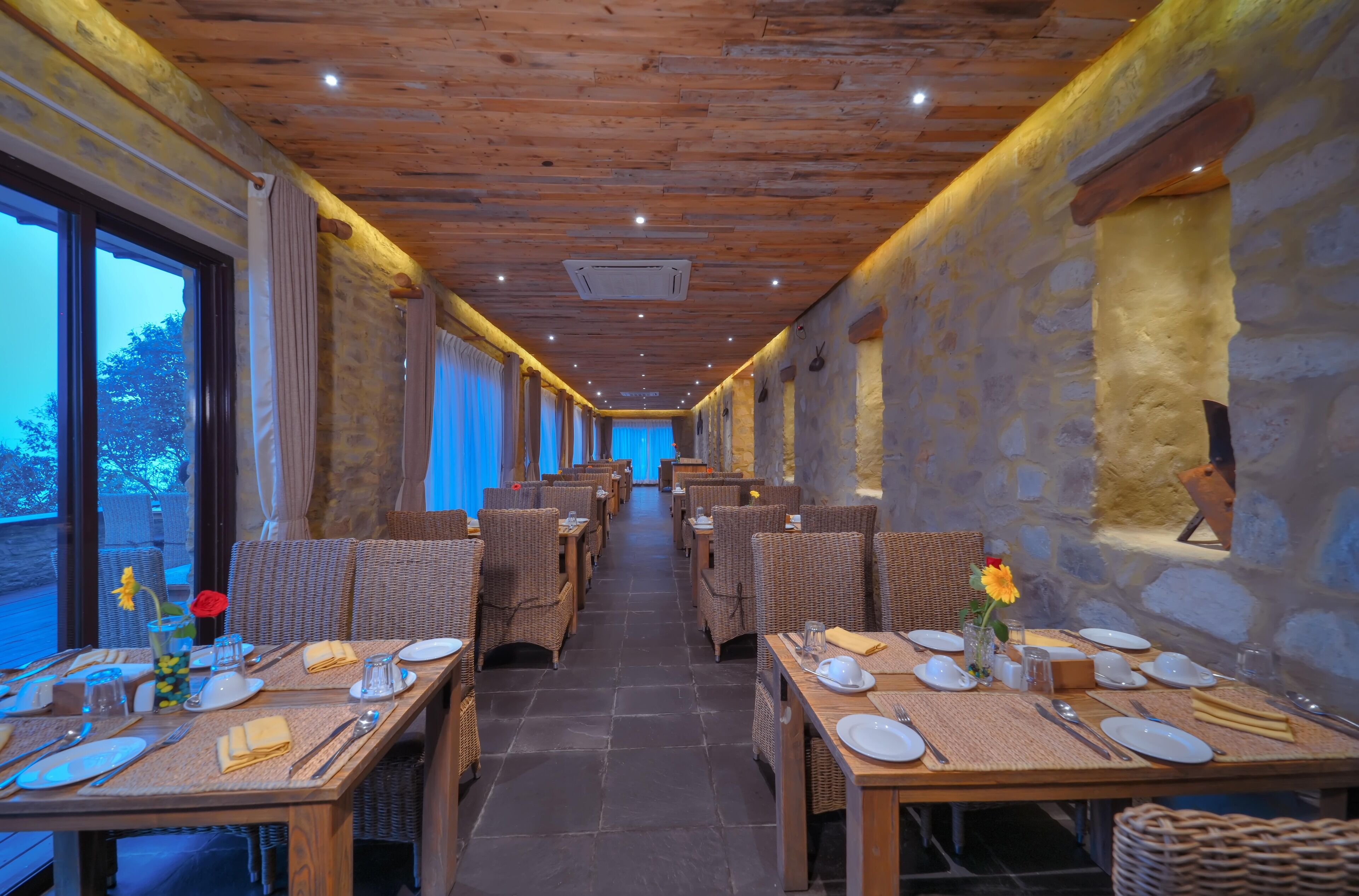 Um restaurante com tetos de madeira e paredes de pedra, com mesas dispostas, pratos, copos e guardanapos.