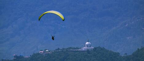 A person paragliding over a mountainous area with a dome-shaped building in the foreground.