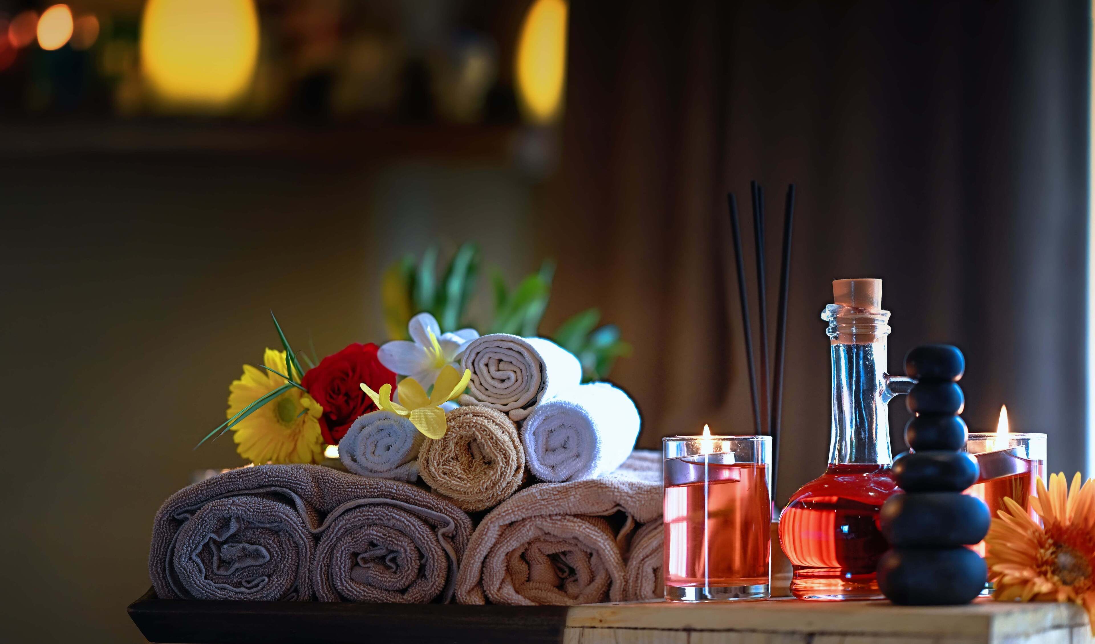 Ein Tisch mit aufgerollten Handtüchern, Kerzen, einer ätherischen Ölflasche und einem Diffusor.