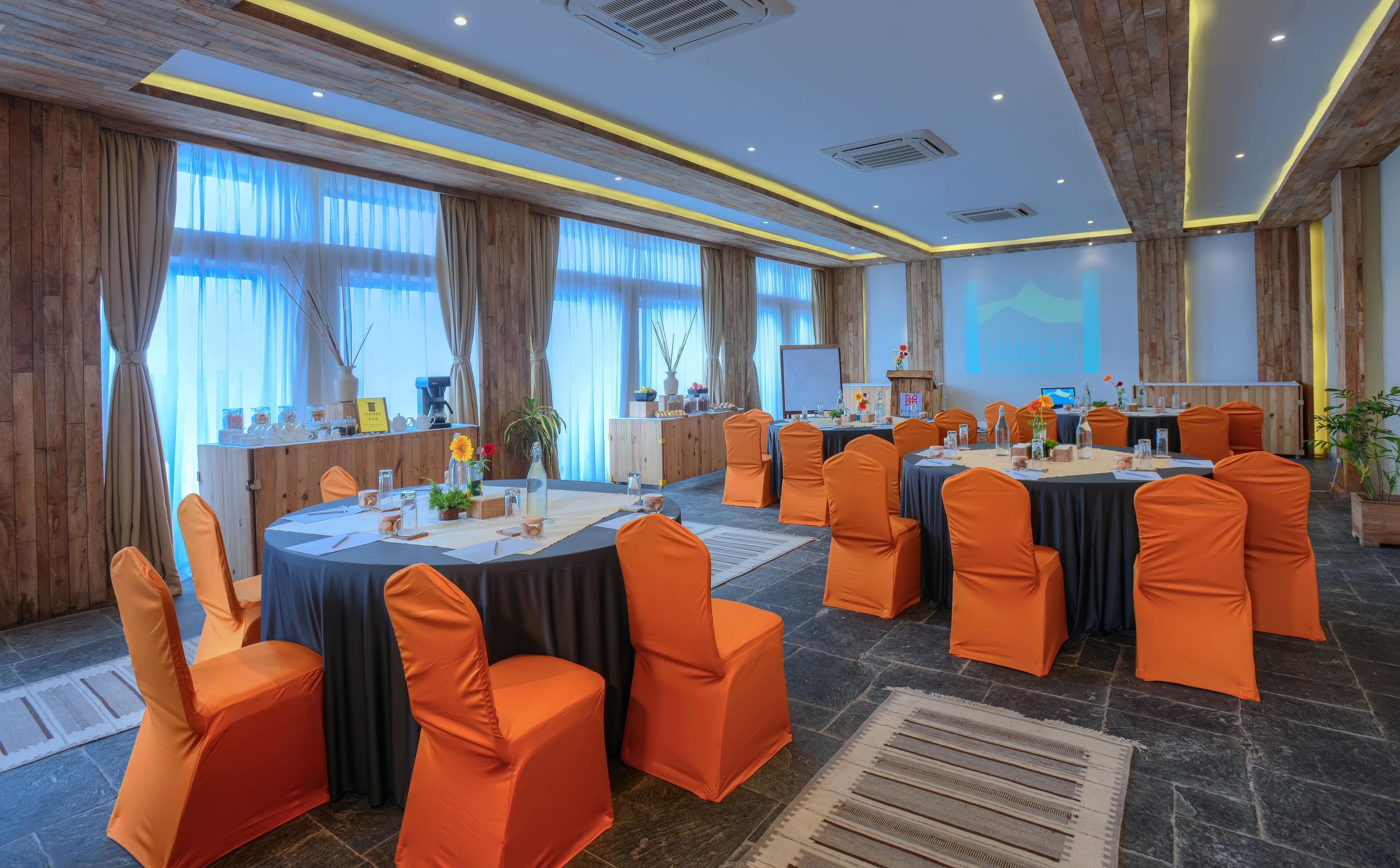 A conference room with round tables, orange chairs, and a projector screen displaying 'SAMPLE IMAGE'.