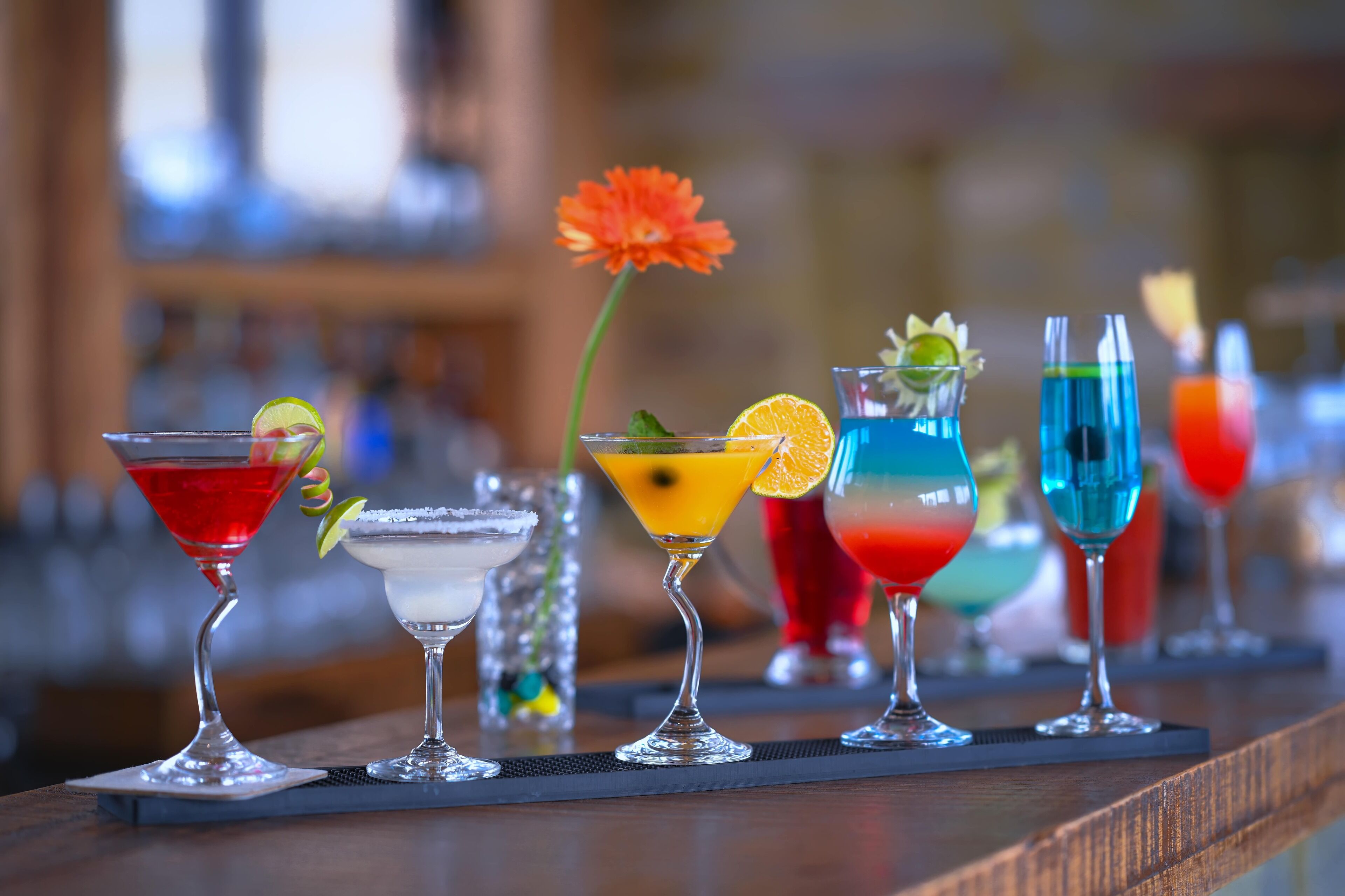 Un bar proposant une variété de cocktails colorés, une fleur et un arrière-plan flou.