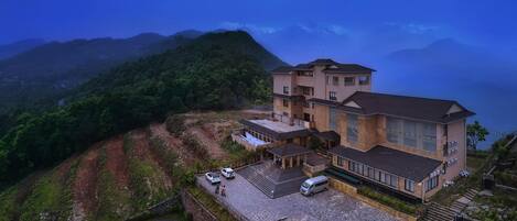 A multi-story building with a large patio area, surrounded by lush greenery and mountains in the background.