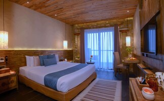 Un dormitorio amplio con una cama grande, cabecera de madera, mesitas de noche, un escritorio con silla, un televisor y una ventana con cortinas.