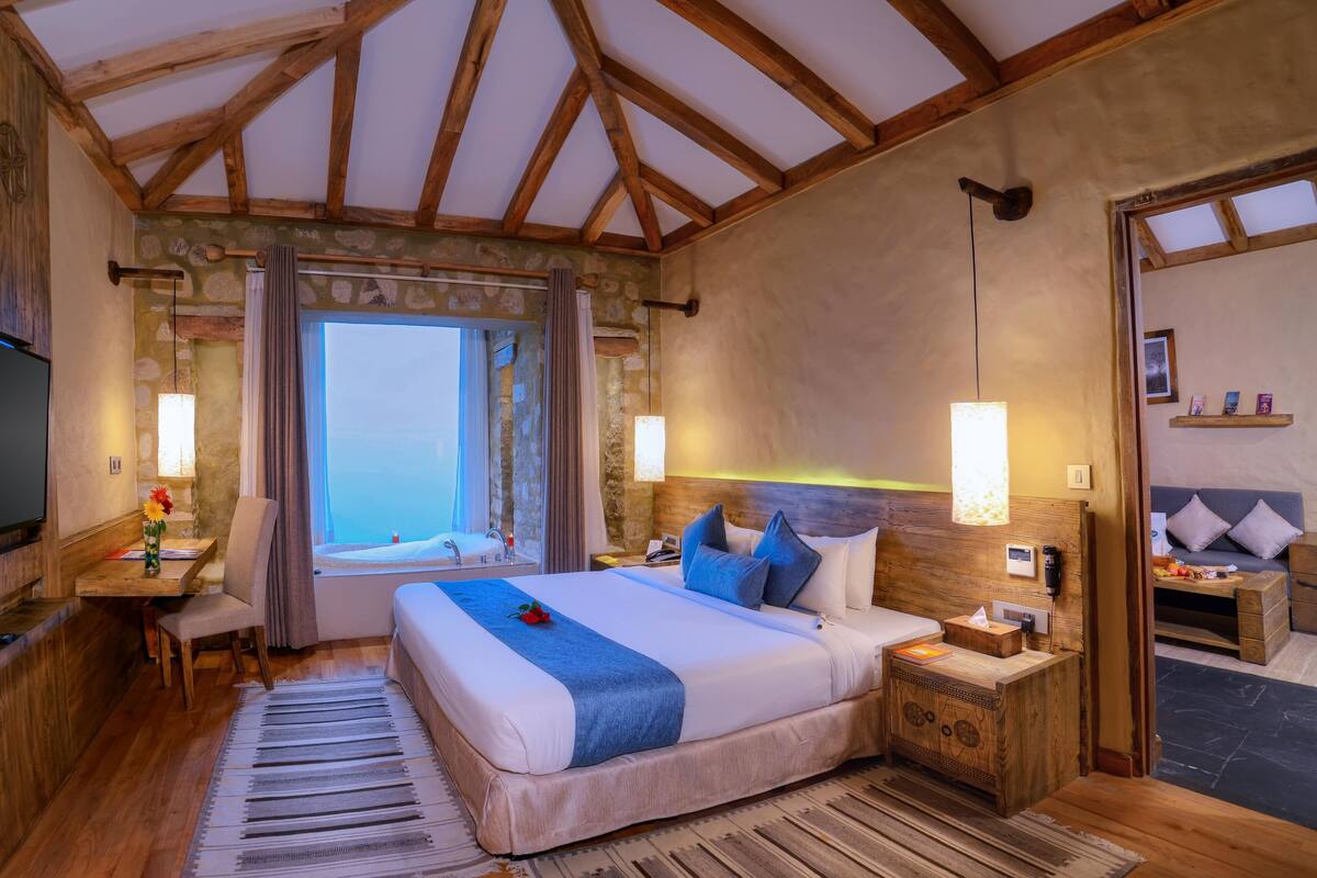 A cozy bedroom with a large bed, a TV, a desk, and a window with a view.