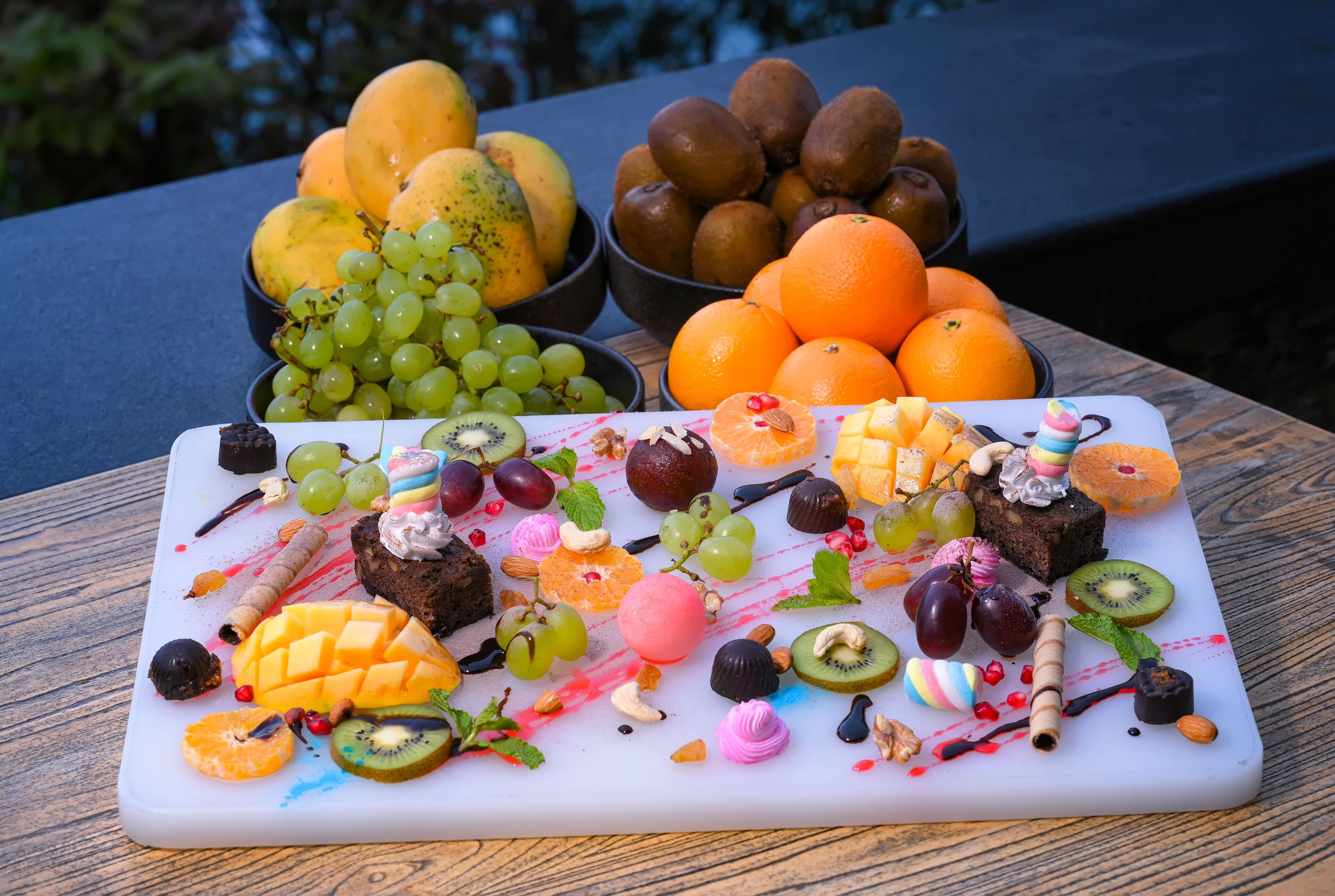 A fruit platter with various fruits and desserts on a wooden table.