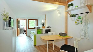 A compact kitchen with a wooden table, white chairs, and a microwave. There are potted plants on the wall and a view of the outdoors through a window. - Bootshaus in Mirow mit überdachter Terrasse (Mirow)