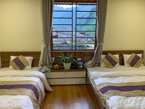A room with two beds, a window with a view of buildings and mountains, and a small table with a plant. - Meo Vac Valley Hotel - Hostel (Meo Vac)