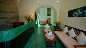 Et hotellobby med grønt tæppe, en receptionsdisk, en sofa og en trappe til et andet rum.