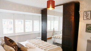 A bedroom with a large bed, a mirror, and a window with blinds. - Zoo Accommodation Chester; 10 min Walk! Sleeps 8 (Upton)