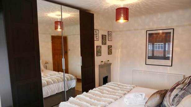 A bedroom with a large mirror, a bed with white bedding, a red pendant light, and framed artwork on the wall. - Zoo Accommodation Chester; 10 min Walk! Sleeps 8 (Upton)
