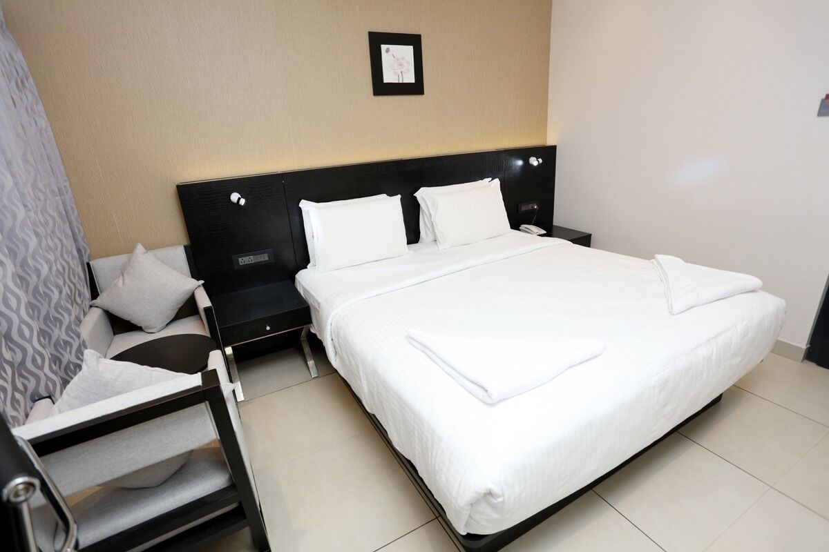Habitación de hotel con una cama grande, una mesita de noche, una silla y un cuadro colgado en la pared.