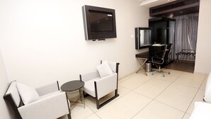 A modern living room with two sofas, a small table, a TV mounted on the wall, and a desk with a chair. - LNB Residency (Tirupati)