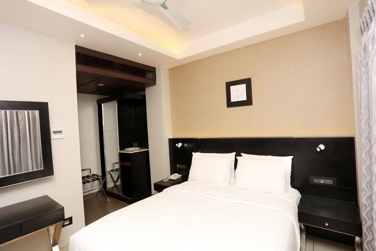 Quarto de hotel com uma cama grande, uma mesa de cabeceira com telefone, cabeceira com painel de controle e um quadro na parede.