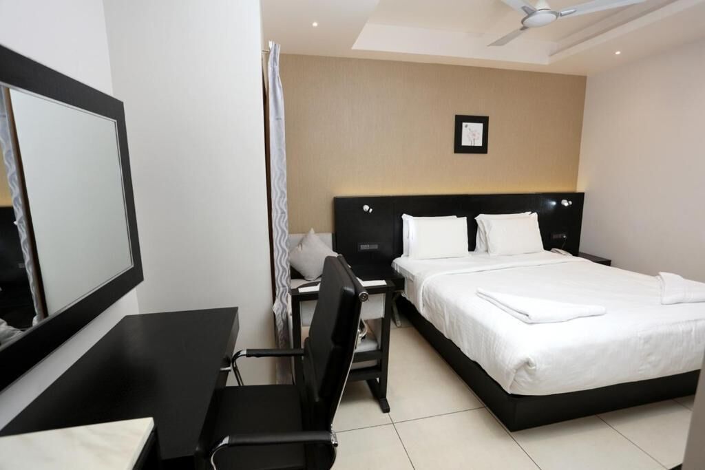 A hotel room with a bed, a desk, a chair, a large mirror, and a ceiling fan.