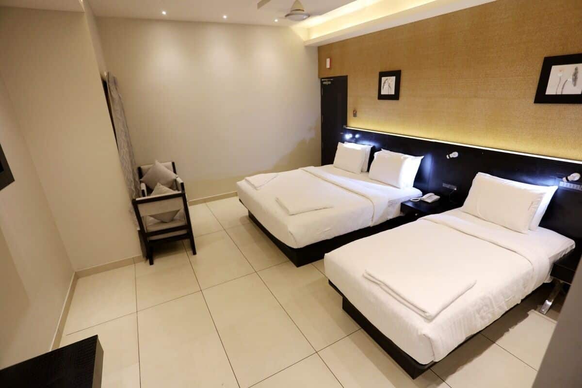Quarto de hotel com duas camas, uma mesinha de cabeceira, uma cadeira e uma obra de arte pendurada na parede.