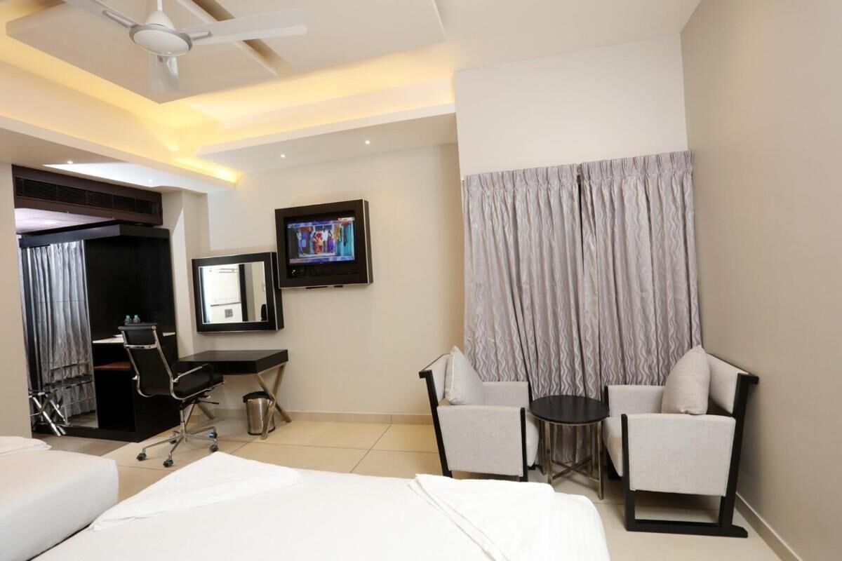 A hotel room with a bed, desk, two chairs, a TV, and a ceiling fan.