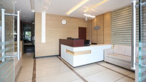 A reception area with a wooden wall, a reception desk, a clock, and a sofa. - LNB Residency (Tirupati)